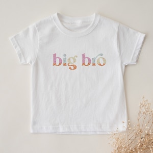 May include: White short-sleeved t-shirt with the text "big bro" in colorful patterned letters.