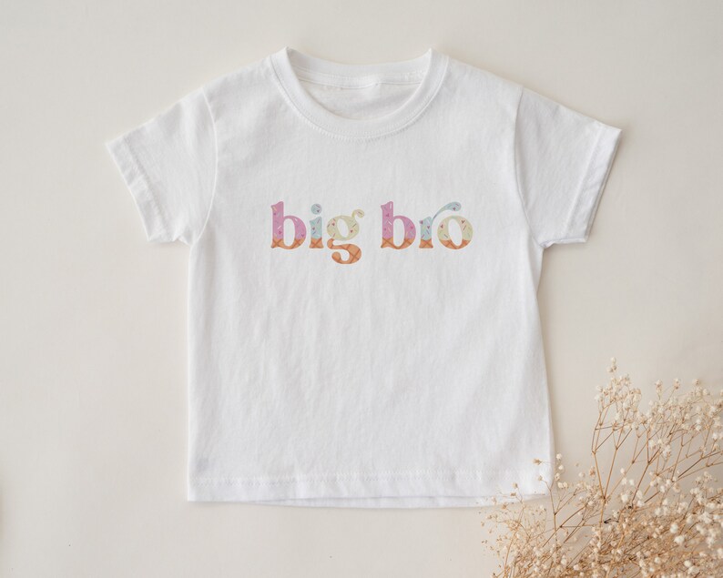 May include: White short-sleeved t-shirt with the text "big bro" in colorful patterned letters.