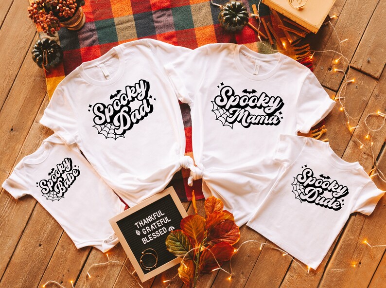 May include: Four white t-shirts with black text and spiderwebs. The shirts say "Spooky Dad", "Spooky Mama", "Spooky Babe", and "Spooky Dude".