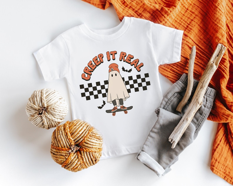May include: White t-shirt with a graphic of a ghost wearing a red beanie and skateboarding. The text "CREEP IT REAL" is above the ghost.