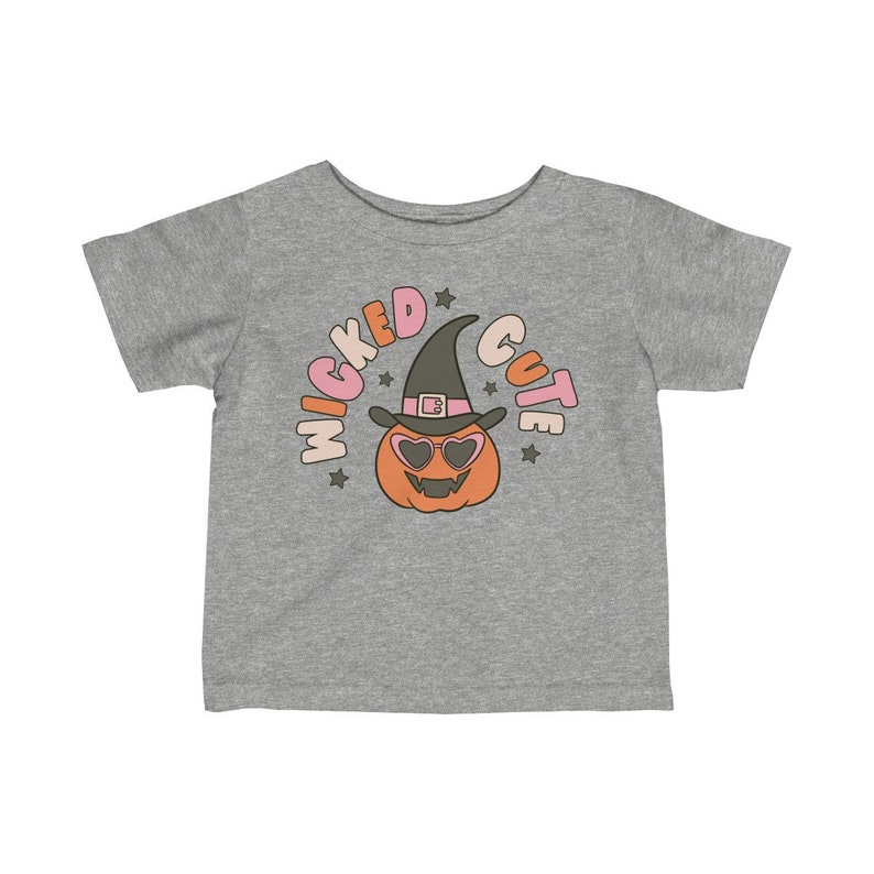 Puede incluir: Una camiseta gris de manga corta con un gr&aacute;fico de una calabaza con un sombrero de bruja y gafas de sol. El texto "Wicked Cute" est&aacute; escrito alrededor de la calabaza en un c&iacute;rculo.