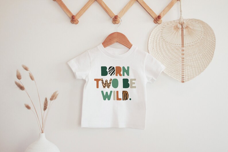 May include: White t-shirt with the text "BORN TWO BE WILD." in colorful letters with animal print patterns.