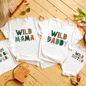 May include: A set of four white t-shirts with a jungle animal theme. The shirts feature the text "Wild Mama", "Wild Daddy", "Born to be Wild", and "Wild Sister".