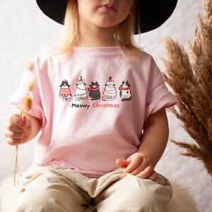 May include: A pink t-shirt with a graphic of five cats wearing Christmas hats and the text "Meowy Christmas".