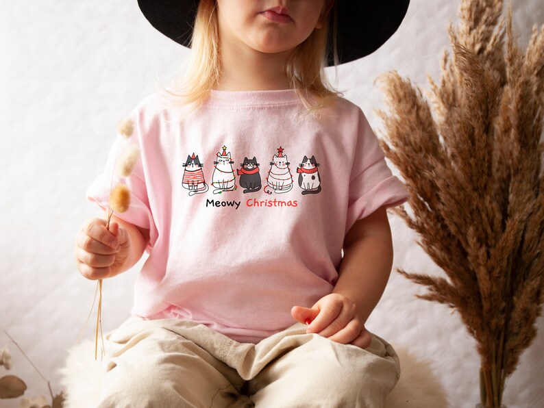 May include: A pink t-shirt with a graphic of five cats wearing Christmas hats and the text "Meowy Christmas".