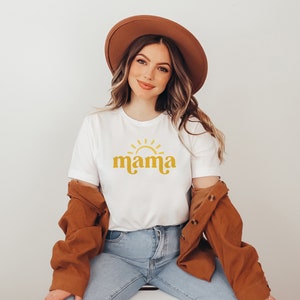 May include: A white t-shirt with a yellow sun and the word "mama" in a retro font.