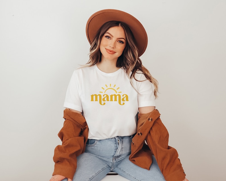 May include: A white t-shirt with a yellow sun and the word "mama" in a retro font.