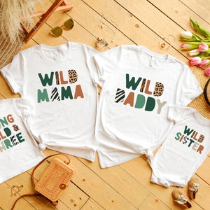 May include: Four white t-shirts with a jungle animal theme. The shirts say "Wild Mama", "Wild Daddy", "Young Wild & Three", and "Wild Sister".