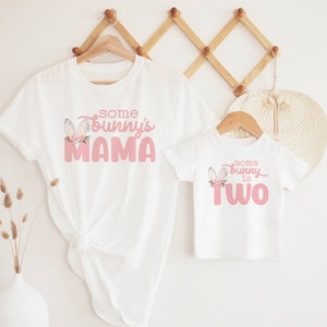 May include: Two white t-shirts with pink bunny ears and text. The larger shirt says "some bunny's mama" and the smaller shirt says "some bunny is two".