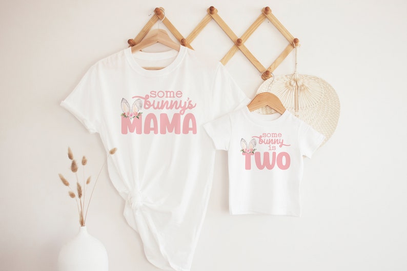 May include: Two white t-shirts with pink bunny ears and text. The larger shirt says "some bunny's mama" and the smaller shirt says "some bunny is two".