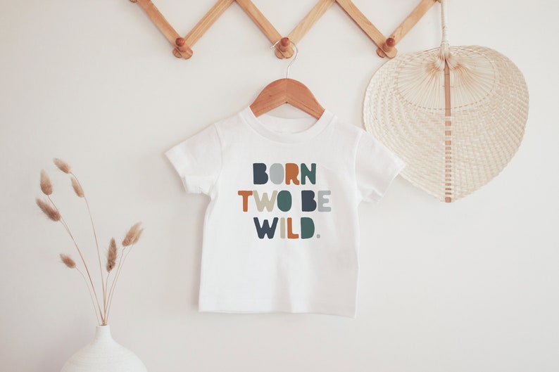 May include: White baby t-shirt with the text "BORN TWO BE WILD." in colorful, rounded letters.