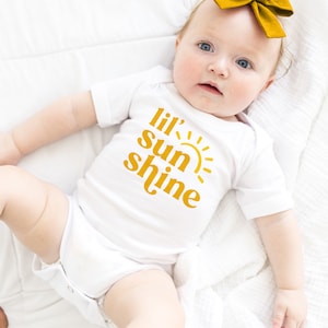 May include: A white baby onesie with a yellow graphic that says "lil' sun shine" and a yellow sun graphic.