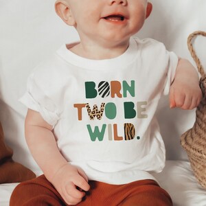 May include: White short-sleeved t-shirt with the text "Born Two Be Wild." in colorful letters with animal print patterns.