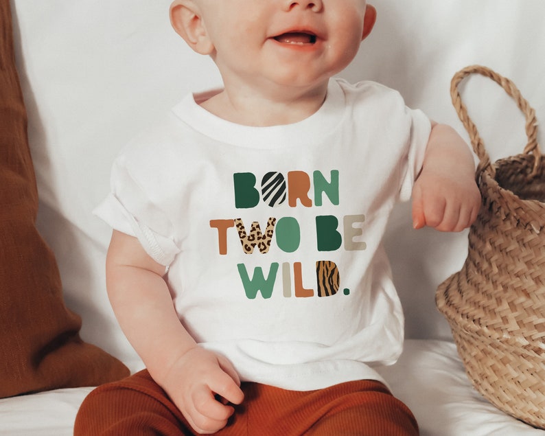 May include: White short-sleeved t-shirt with the text "Born Two Be Wild." in colorful letters with animal print patterns.