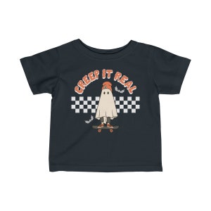 May include: A dark blue toddler t-shirt with a white ghost wearing an orange beanie and skateboarding. The ghost is in front of a black and white checkered pattern with the text "CREEP IT REAL" in orange.