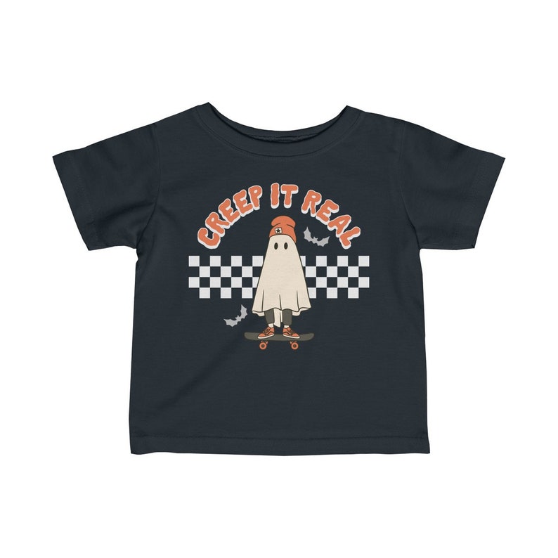 May include: A dark blue toddler t-shirt with a white ghost wearing an orange beanie and skateboarding. The ghost is in front of a black and white checkered pattern with the text "CREEP IT REAL" in orange.
