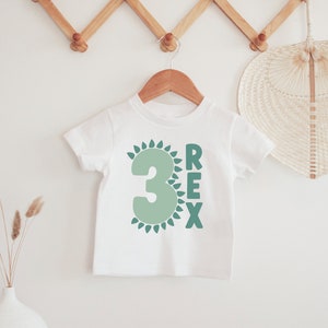 May include: White t-shirt with a green number 3 surrounded by green leaves and the word "REX" in green letters.