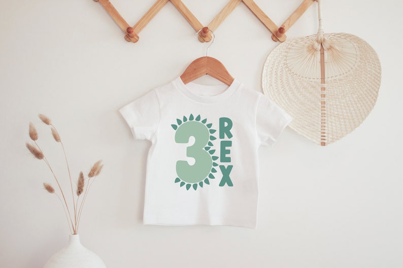 May include: White t-shirt with a green number 3 surrounded by green leaves and the word "REX" in green letters.