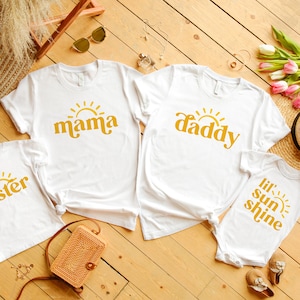 May include: Four white t-shirts with a yellow sun and text. The shirts say "mama", "daddy", "sister", and "lil' sun shine".