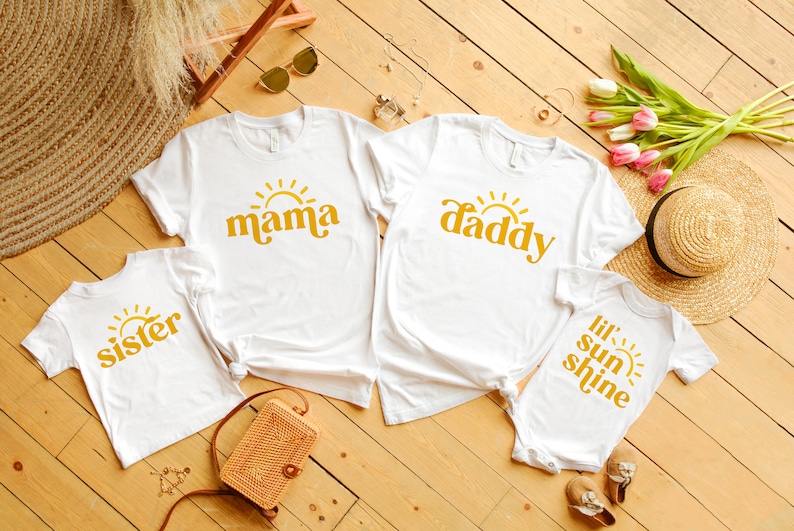 May include: Four white t-shirts with a yellow sun and text. The shirts say "mama", "daddy", "sister", and "lil' sun shine".