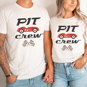 May include: Two white t-shirts with a red race car graphic and the text "PIT crew" printed on them. The shirts are being worn by two people.