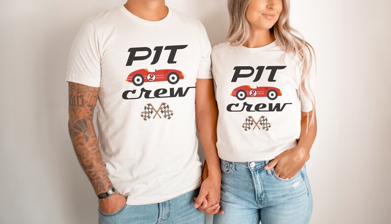 May include: Two white t-shirts with a red race car graphic and the text "PIT crew" printed on them. The shirts are being worn by two people.