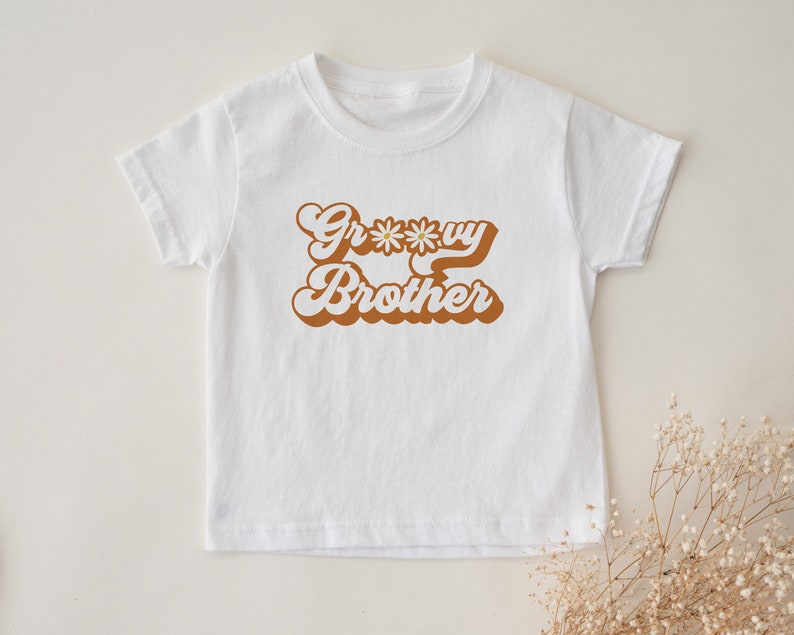 May include: White t-shirt with brown text that says "Groovy Brother" with a daisy graphic.
