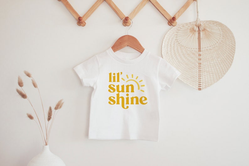 May include: White baby onesie with a yellow graphic that says "Lil' sun shine" with a stylized sun graphic.
