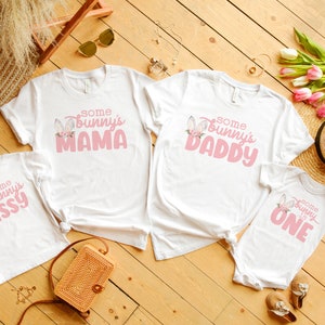 May include: Four white t-shirts with pink text and bunny graphics. The shirts say "Some Bunny's Mama", "Some Bunny's Daddy", "Some Bunny's Sissy", and "Some Bunny is One".
