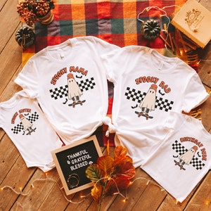 May include: Four white t-shirts with a ghost skateboarding graphic. The shirts say "Spooky Mama", "Spooky Dad", "Spooky Sister", and "Birthday Dude".