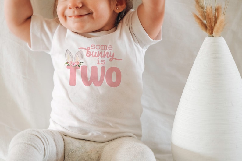 May include: A white t-shirt with a pink bunny graphic and the text "some bunny is two".
