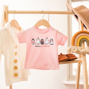May include: Pink toddler t-shirt with a graphic of five cats wearing Christmas hats and the text "Meowy Christmas".