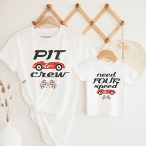 K&ouml;nnte beinhalten: Zwei wei&szlig;e T-Shirts mit einem roten Rennwagen-Motiv. Das gr&ouml;&szlig;ere Shirt sagt "PIT crew" und das kleinere Shirt sagt "need FOUR speed".