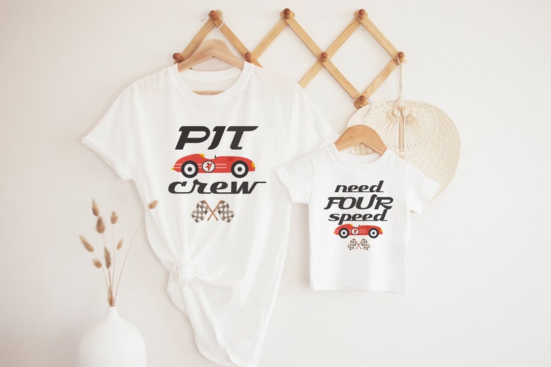 K&ouml;nnte beinhalten: Zwei wei&szlig;e T-Shirts mit einem roten Rennwagen-Motiv. Das gr&ouml;&szlig;ere Shirt sagt "PIT crew" und das kleinere Shirt sagt "need FOUR speed".