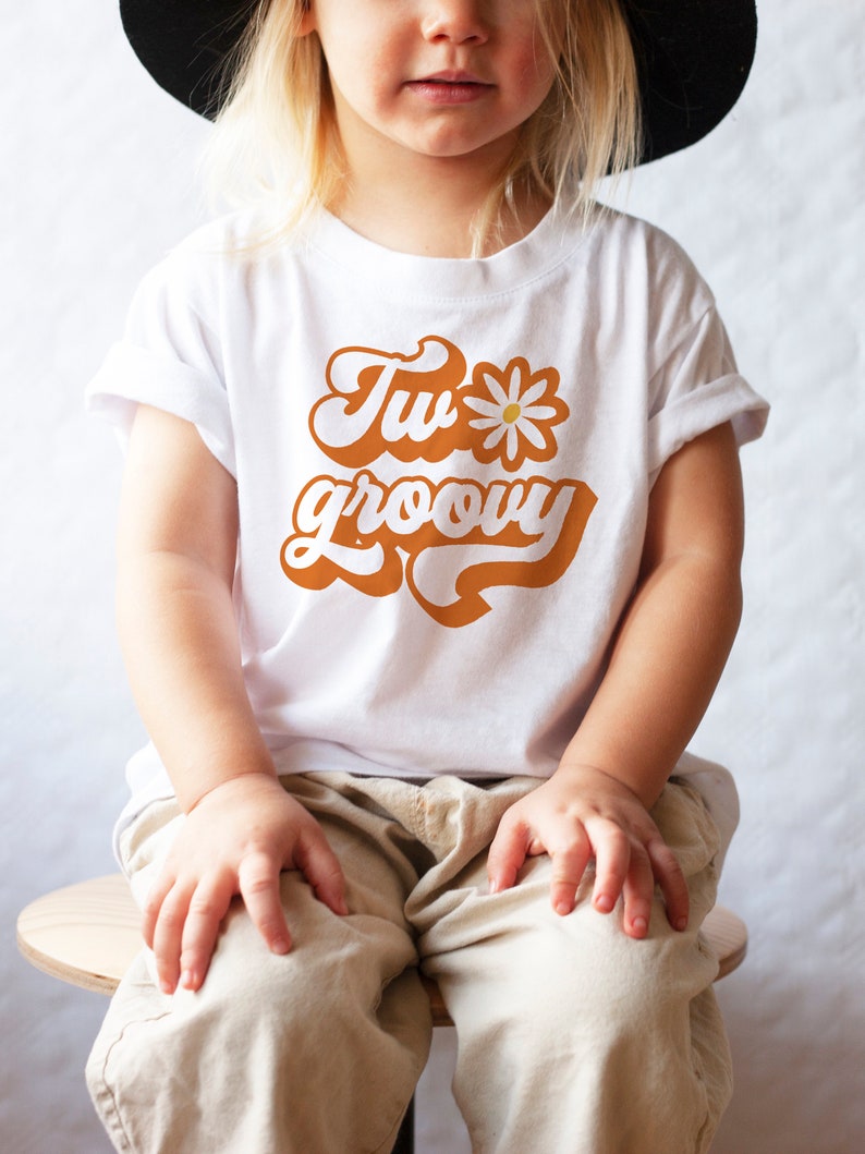 May include: A white t-shirt with a retro-style orange graphic that says "Two groovy" with a white daisy.