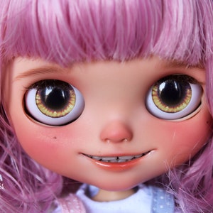 May include: A close-up of a doll's face with pink hair, large brown eyes with yellow irises, and a slight smile. The doll is wearing braces and has rosy cheeks. The text 'ANYA PUPPET TALES' is visible at the bottom of the image.