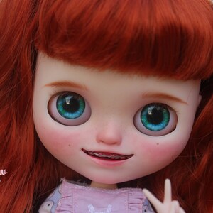 May include: A doll with red hair, blue eyes, and a pink and gray dress. The doll is smiling and has braces on her teeth. The text 'Willow Puppet Tales' is visible at the bottom of the image.