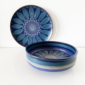 May include: Two blue and purple ceramic bowls with a floral design. The larger bowl has a wide rim and a smaller bowl is nested inside.