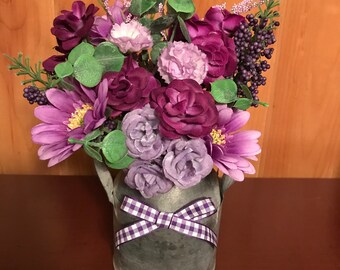 May include: A purple and white flower arrangement in a galvanized metal pitcher with a purple and white checkered ribbon.