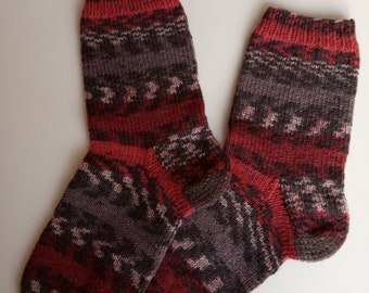 May include: A pair of hand-knitted socks with a patterned design. The socks feature a colour palette of red, grey, and white. The cuff, heel, and toe are a solid red, while the body has a geometric pattern.