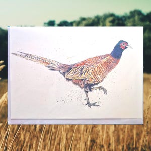 May include: A watercolor illustration of a pheasant on a greeting card. The bird is depicted in shades of brown, orange, and black, with a blue head and red eye. The pheasant is shown mid-stride against a white background.