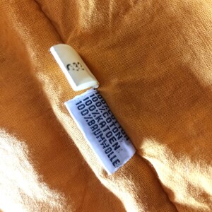 May include: Close-up of a textured, orange fabric with a white tag and a small, white rectangular piece. The tag reads "100% COTON, 100% KATOEN, 100% BAUMWOLLE". The small piece has the number "032" printed on it.