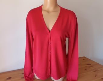 May include: A bright red cardigan sweater with a V-neck and long sleeves. The sweater has a button-up front and is displayed on a mannequin. The garment is made of a soft material and is suitable for layering.