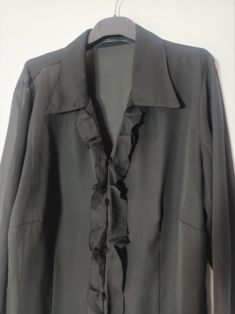 May include: A black long-sleeved blouse with a ruffled front and button closure.