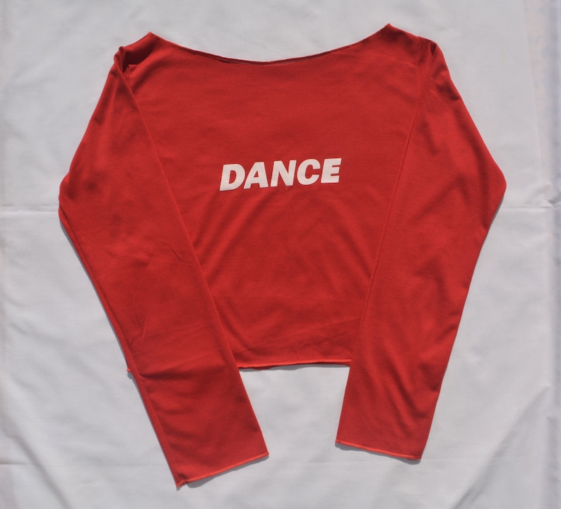 May include: Red long-sleeved shirt with a boat neck and the word "DANCE" printed in white on the front.