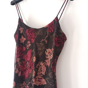 Peut inclure: Une robe noire en satin avec un imprim&eacute; floral rouge, rose et marron. La robe a des bretelles fines et un col rond.