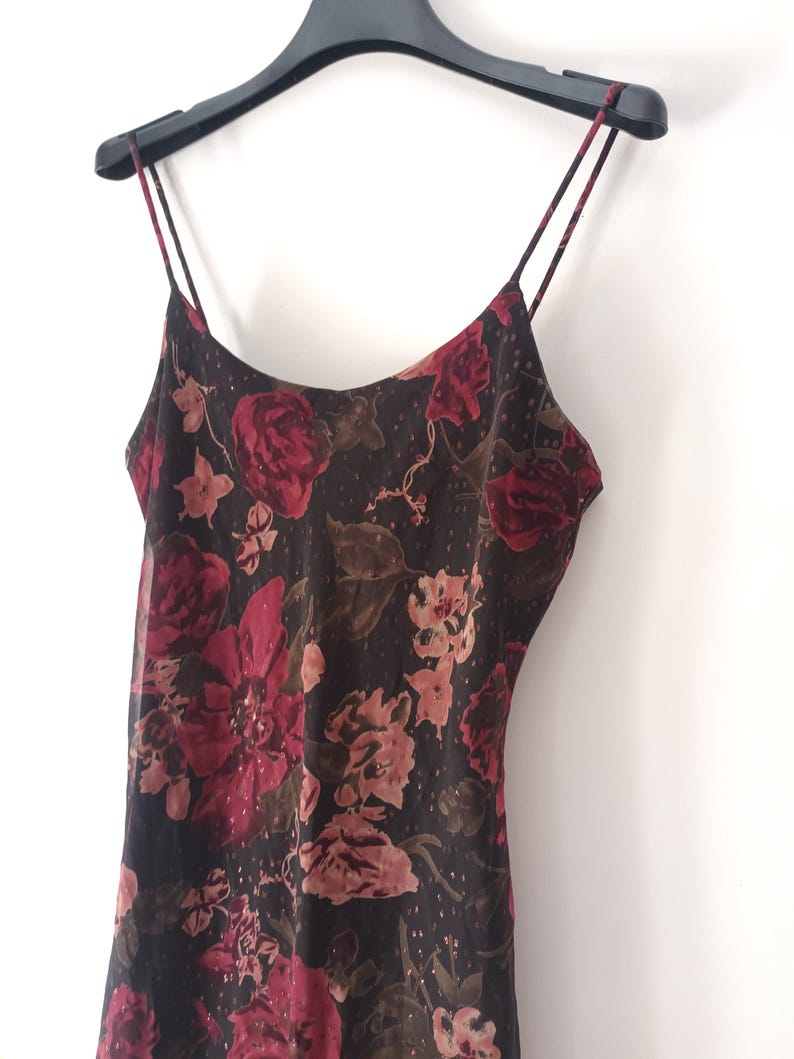 Peut inclure: Une robe noire en satin avec un imprim&eacute; floral rouge, rose et marron. La robe a des bretelles fines et un col rond.