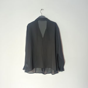 May include: A black sheer blouse with long sleeves and a V-neckline. The blouse has a ruffled hem and a sheer overlay at the neckline.