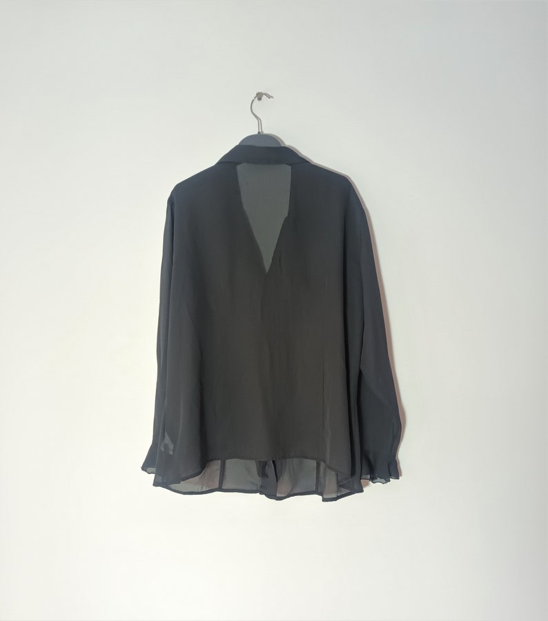 May include: A black sheer blouse with long sleeves and a V-neckline. The blouse has a ruffled hem and a sheer overlay at the neckline.