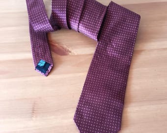 May include: A burgundy tie with a repeating white dot pattern. The tie is made of a smooth fabric and is displayed on a wooden surface. The tie is a classic accessory for formal or business attire.